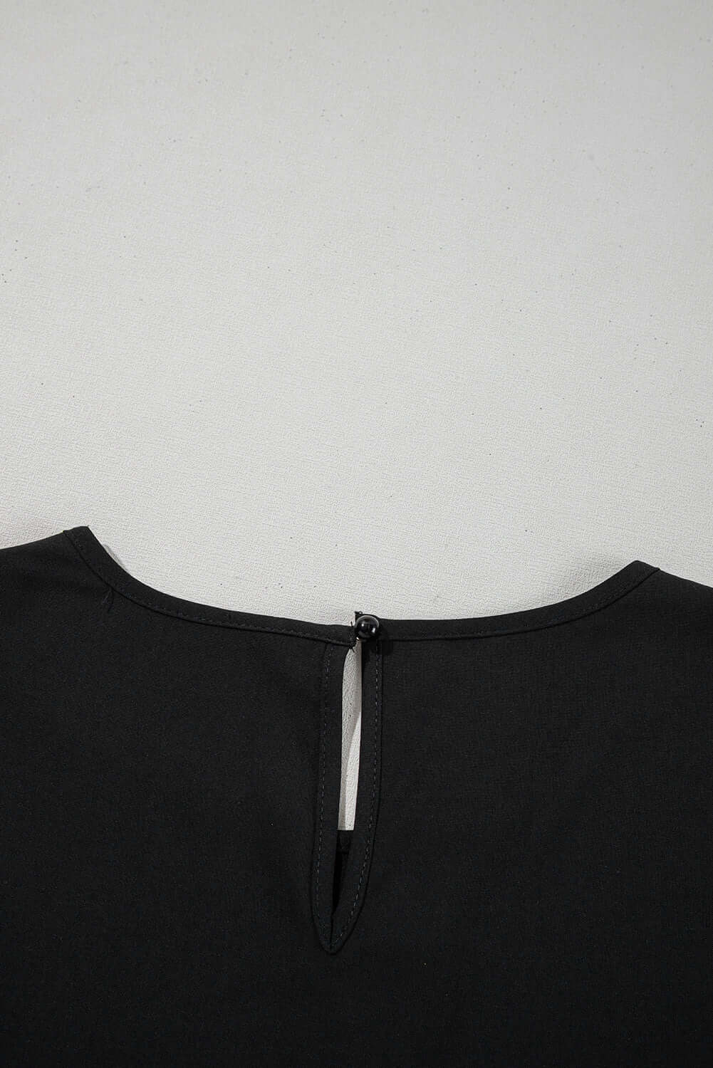 Back view of the black Fringe Benefits top featuring a keyhole opening and zipper detail.