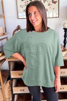 Woman wearing sea green Flower Theory Top with oversized floral design and relaxed fit.