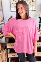 Woman wearing Flower Theory Top in taffy pink with oversized floral design, showcasing casual style and comfort.