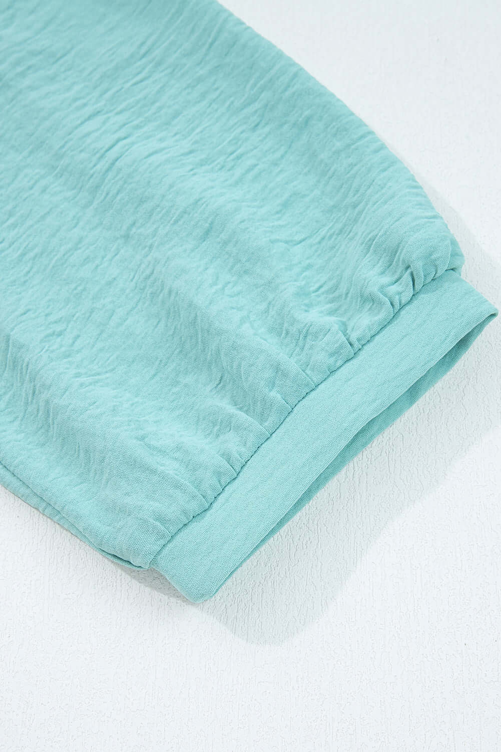 Close-up of the sleeve of the GRACEFUL GLOW TOP (jade sea) showcasing its crinkled fabric texture and elegant design.