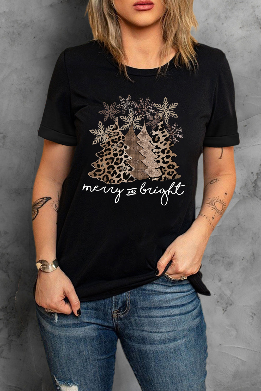 Woman wearing black Merry & Bright Leopard Tee with festive Christmas tree graphic and leopard print, paired with blue jeans.