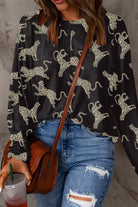 Woman wearing a long-sleeved black top with a cheetah print design, paired with distressed jeans and holding a drink.