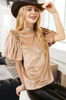 Woman wearing champagne velvet blouse with ruffled puff sleeves and mock neck, styled with a hat for a chic date night look.