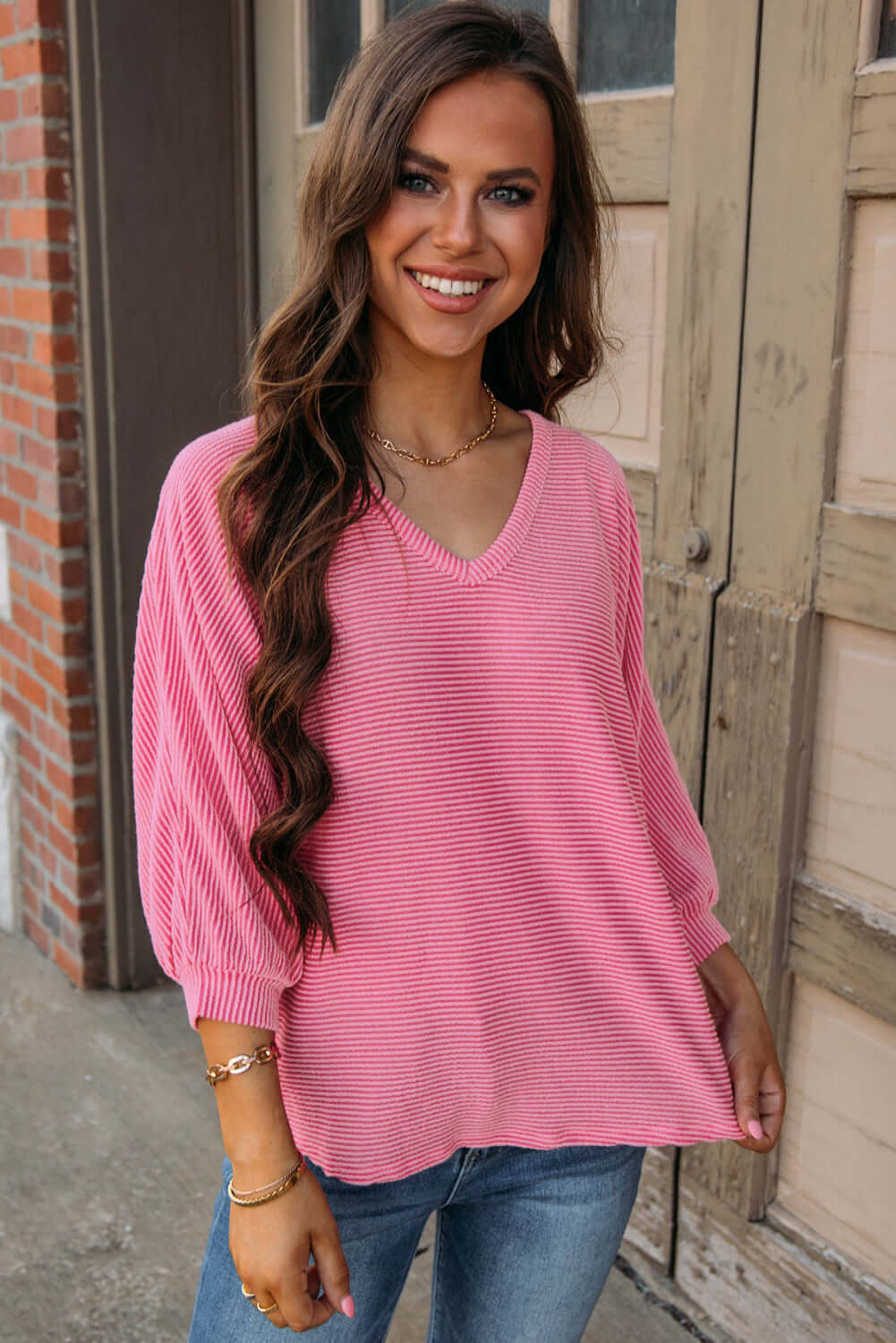 Young woman wearing a pink striped HAPPY THOUGHTS top by Vivian-Lu, featuring a v-neck and bracelet sleeves.