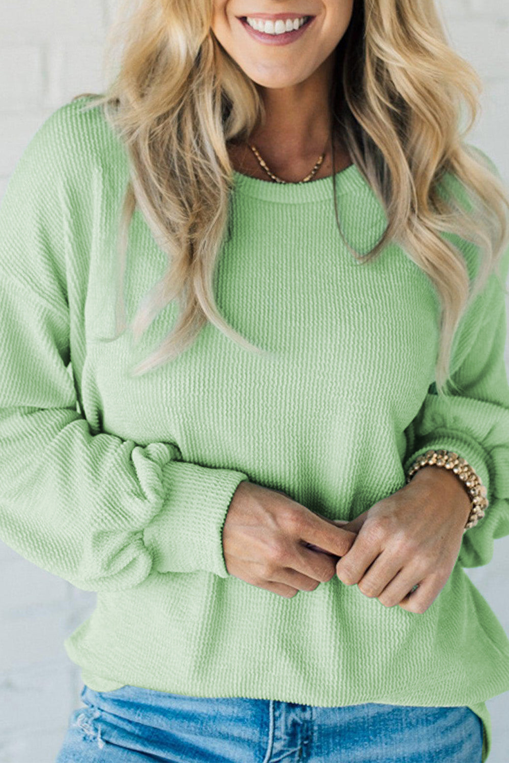 Woman wearing a mint green corded ribbing top with drop shoulder design and relaxed fit, paired with blue jeans for a casual look.