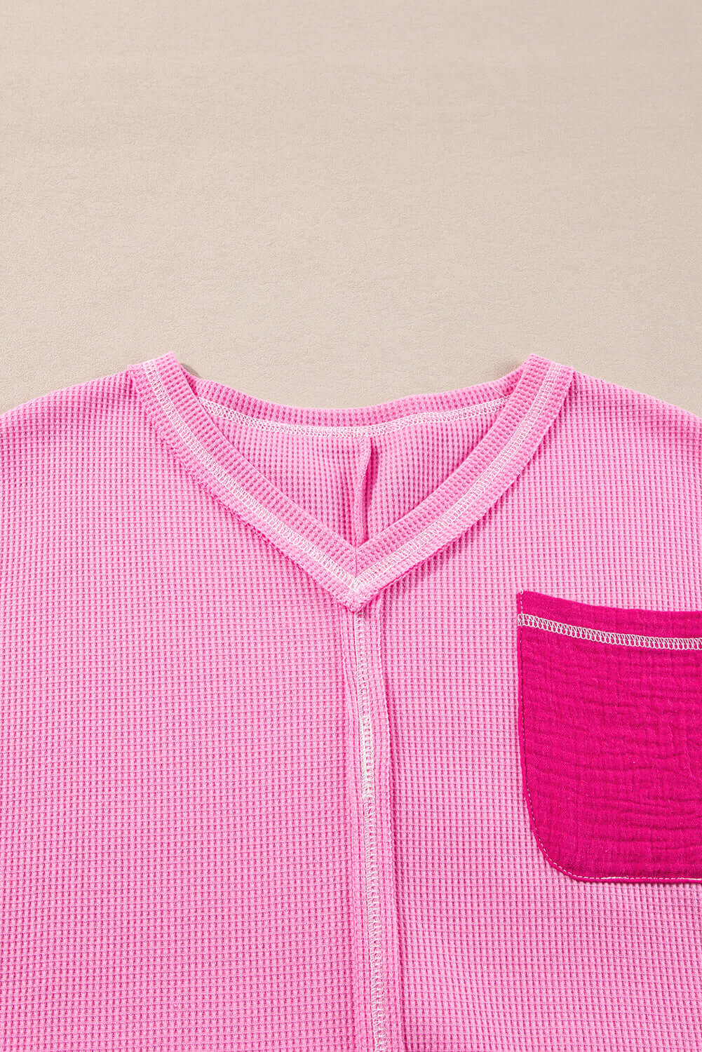 Close-up of a pink ribbed top featuring a V-neck and contrasting pocket detail.