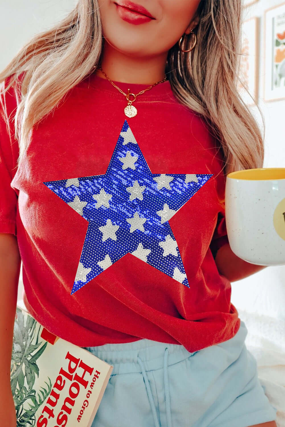 Woman wearing a red tee with a blue sequin star graphic, holding a mug and a magazine.