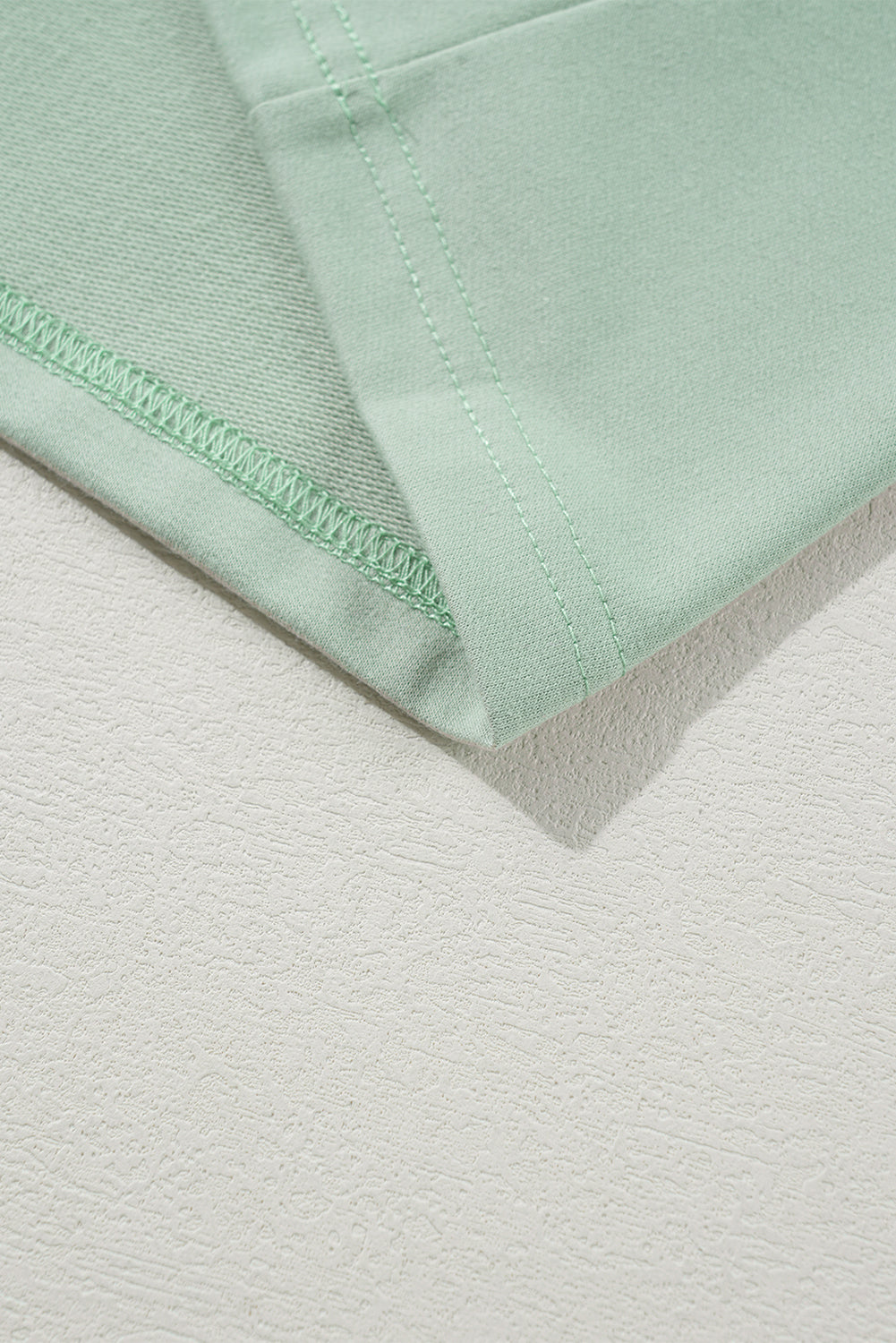 Close-up of sage green fabric with stitched hem detail.