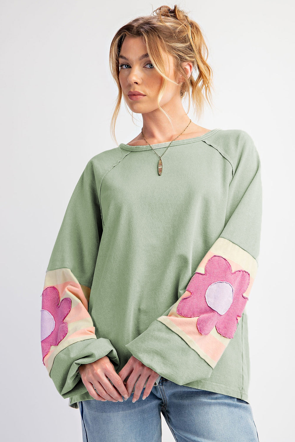 Sage oversized pullover with pink floral sleeve accents, vintage flair, and raw cut details, perfect for casual wear.