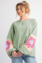 Sage oversized pullover with pink floral sleeve accents, vintage flair, and raw cut details, perfect for casual wear.