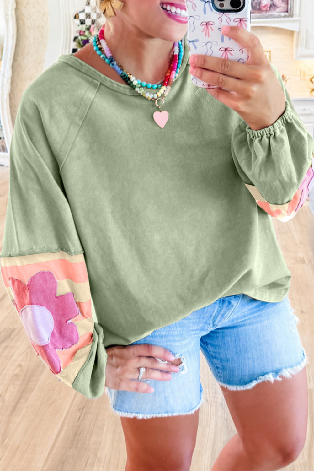 Sage oversized pullover with vintage flair, bubble sleeves, and colorful stripe pattern, worn casually with denim shorts.