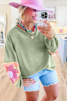 Woman wearing sage oversized pullover with vintage flair, bubble sleeves, and colorful stripes, paired with denim shorts and pink hat.