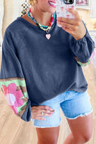 Woman wearing a stylish blue oversized pullover with vintage flair, colorful sleeve patterns, and raw cut details, paired with denim shorts.