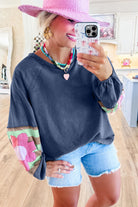 Woman wearing oversized pullover with vintage flair, featuring bubble sleeves with floral pattern and raw cut details, paired with denim shorts.