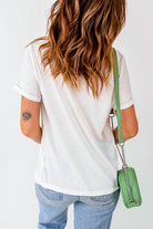 Woman with long hair wearing a white cuffed sleeve t-shirt and blue jeans, holding a green purse with chain strap.