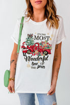 Woman wearing a "Most Wonderful Time" T-shirt with red truck and gifts design, cuffed sleeves, and a crew neck for holiday spirit.