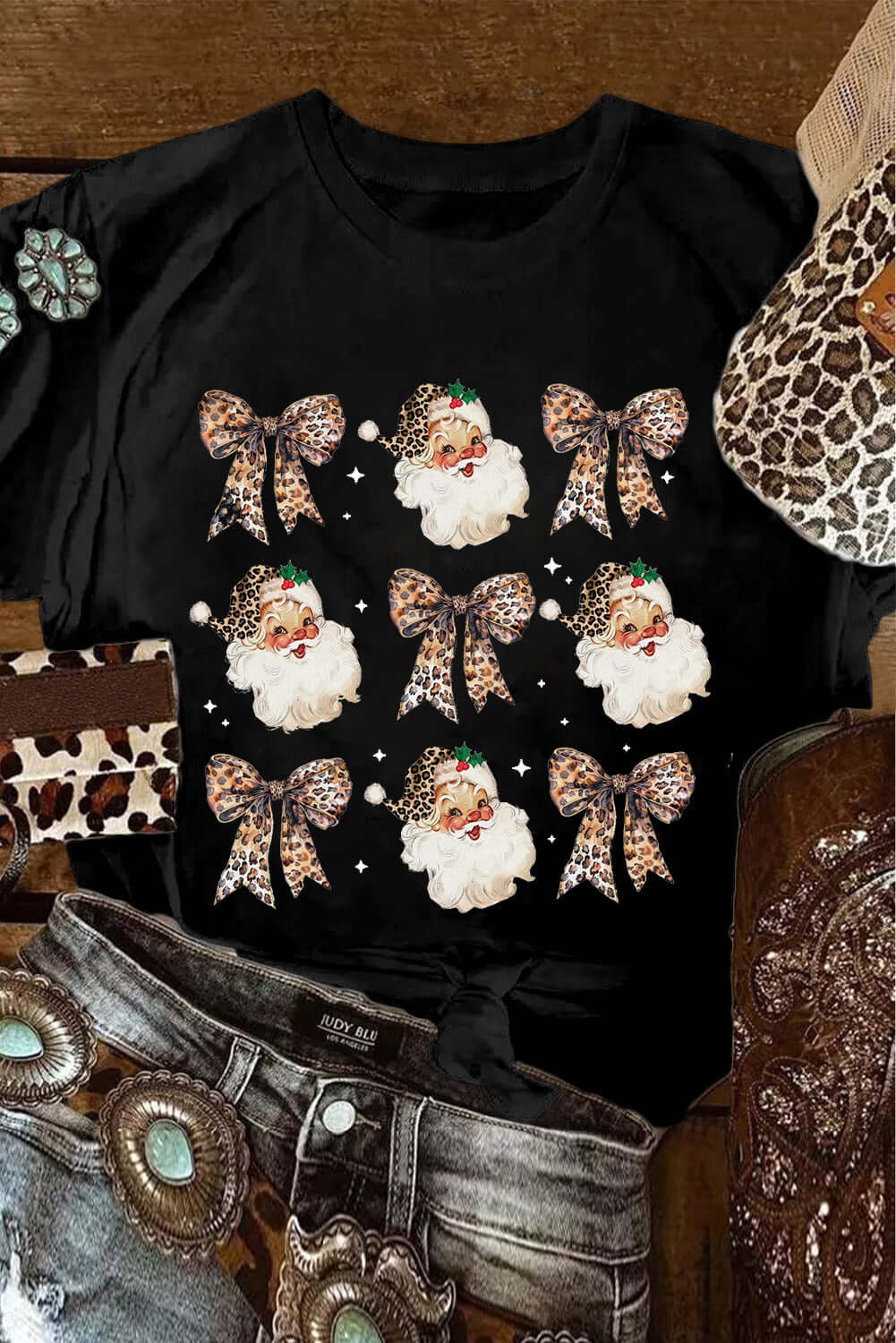 Festive black T-shirt with leopard print bows and Santa Claus graphics, styled with denim jeans for a chic holiday look.