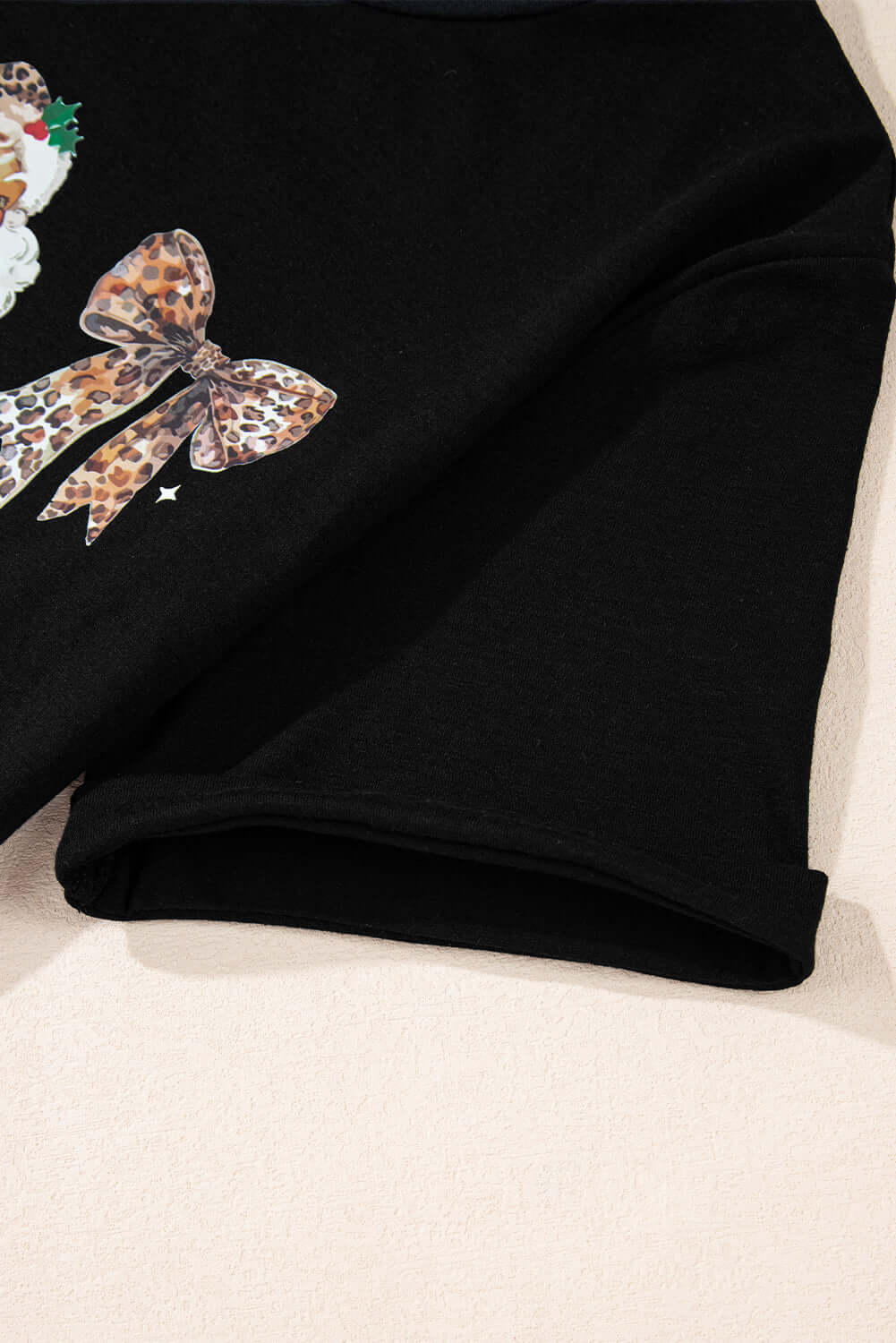 Close-up of HO HO HO AND BOWS T-shirt featuring leopard print bow on soft black fabric.