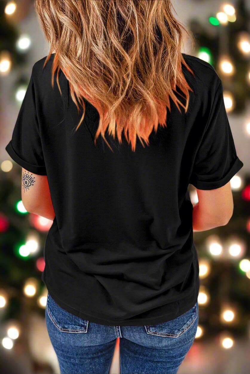 Woman wearing a black T-shirt with holiday lights in the background, showcasing casual holiday fashion.