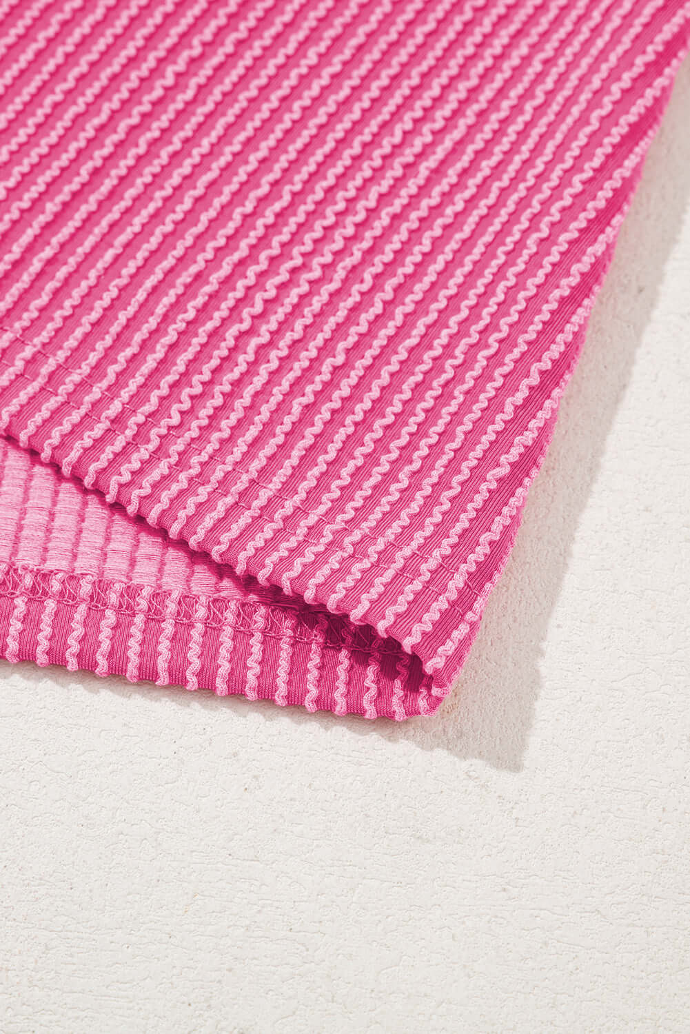 Close-up of hot pink corded knit fabric, showcasing its striped texture and vibrant color pattern.