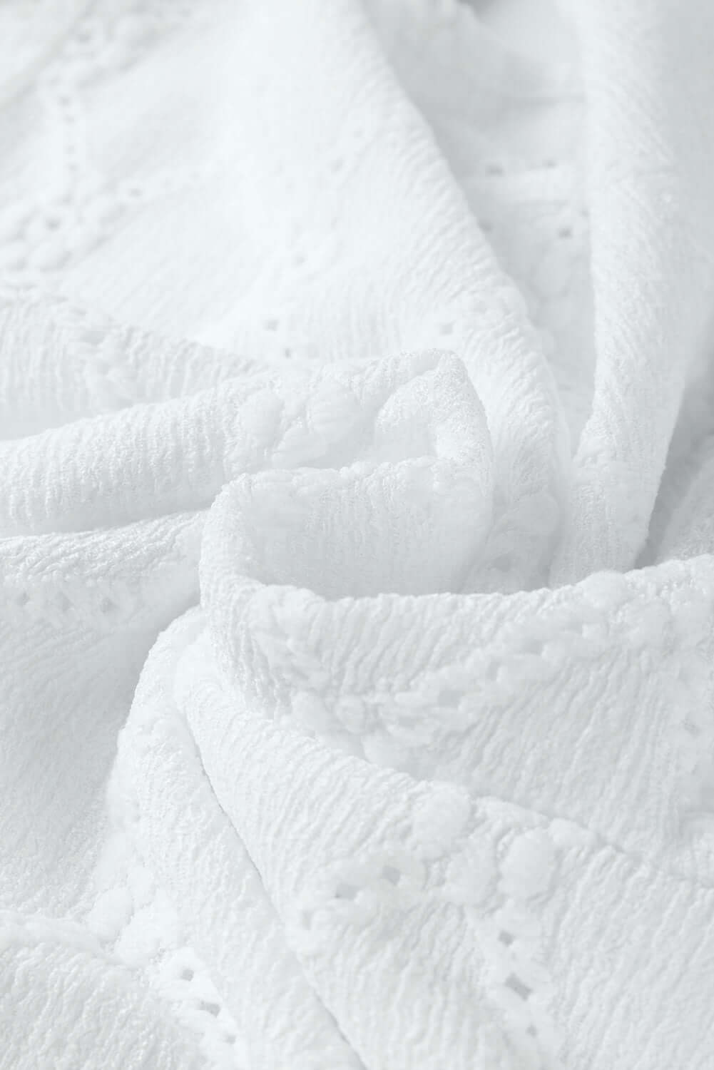 Textured white fabric showcasing delicate floral and geometric lace patterns for elegant fashion.