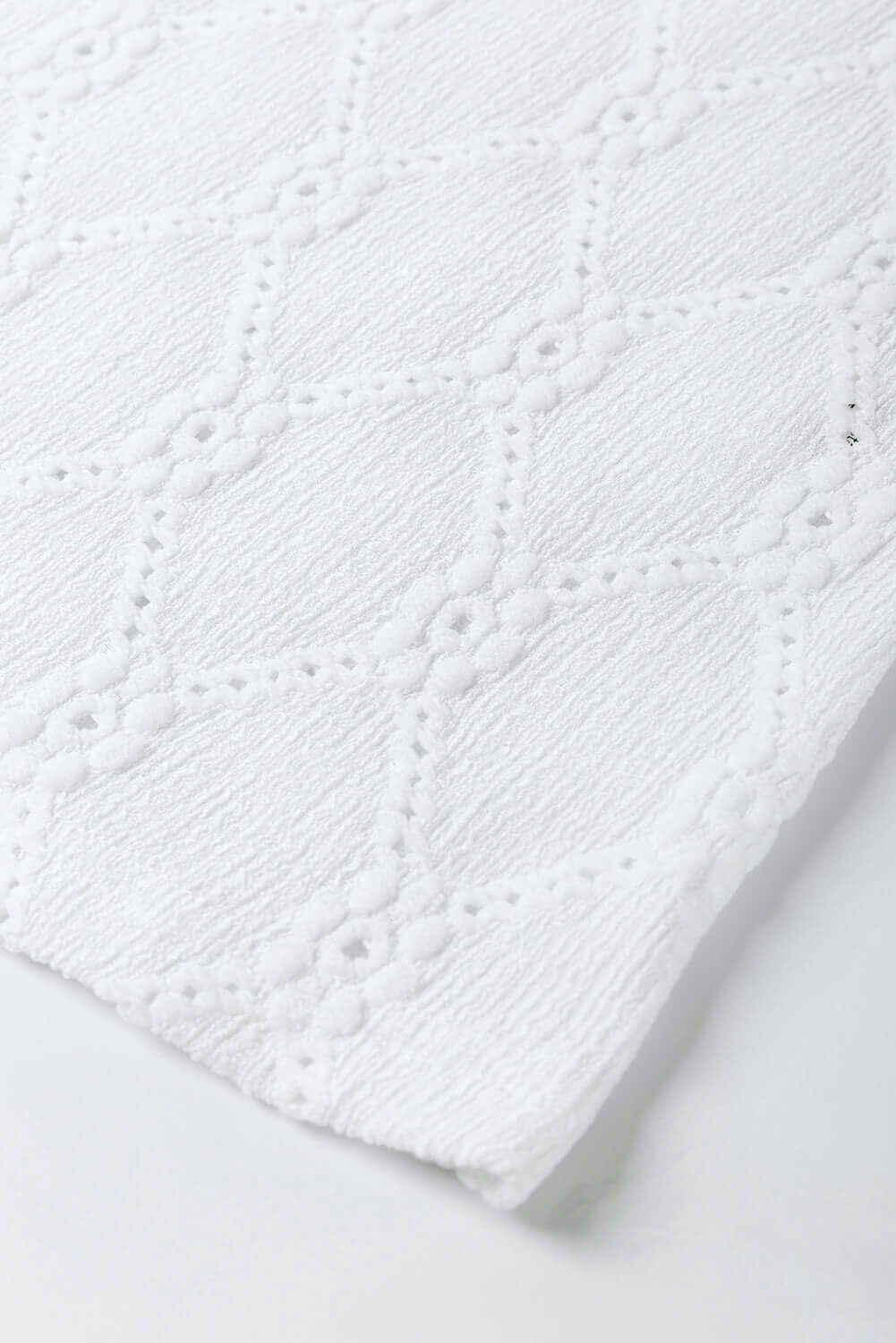Close-up of white textured fabric featuring a floral and geometric lattice design.