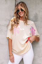 Woman wearing a relaxed vanilla top with floral patches, styled with sunglasses and white jeans.