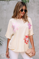Woman wearing a vanilla floral patch top with relaxed fit and exposed stitching against a neutral background.