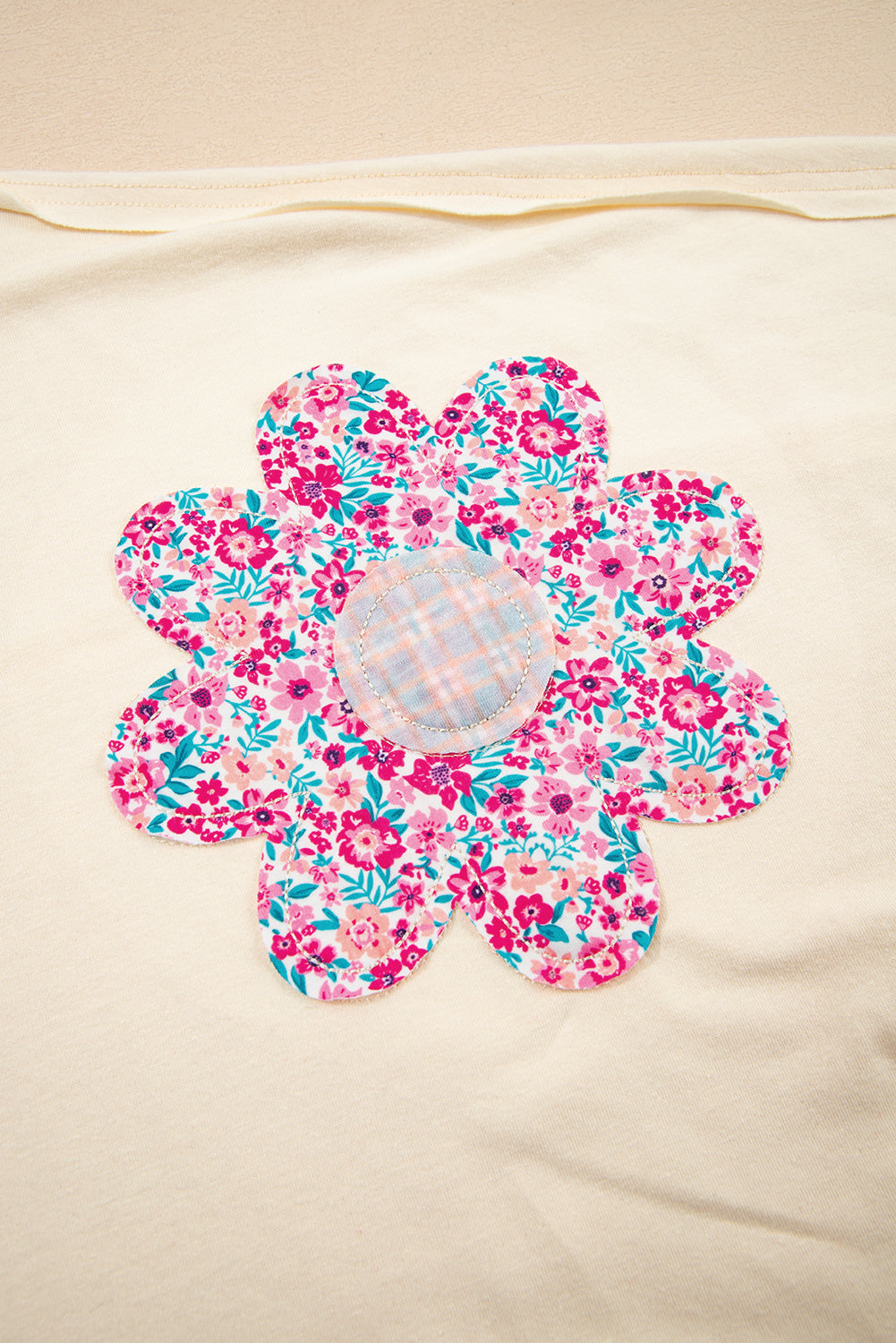 Close-up of a colorful floral patch on a vanilla top, featuring pink and blue floral designs.
