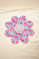 Close-up of a colorful floral patch on a vanilla top, featuring pink and blue floral designs.