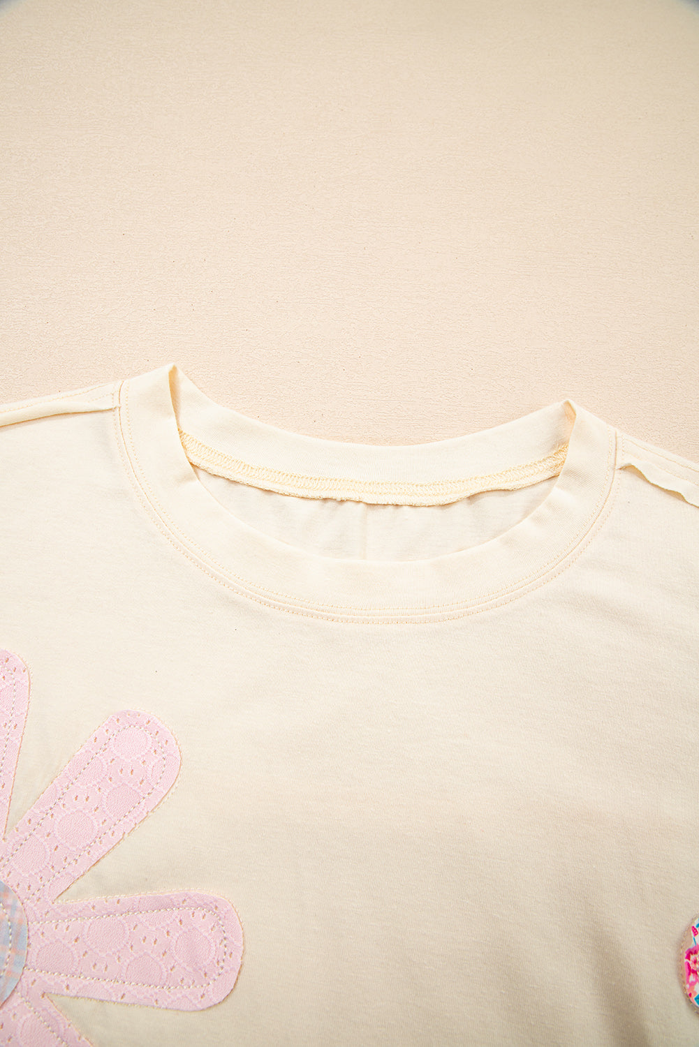 Vanilla cream tee with floral patches and exposed stitching, perfect for a relaxed, stylish look.