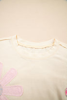 Vanilla cream tee featuring playful floral patches and exposed stitching for a stylish boutique look.