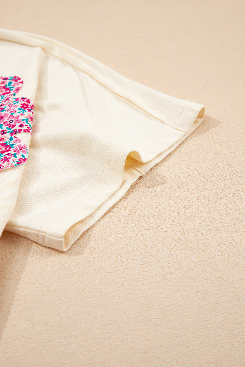 Vanilla cream shirt with floral patch and exposed stitching detail on a soft background.