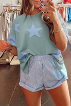 Oversized sage star patch tee with frayed details styled with striped shorts in a trendy boutique setting.