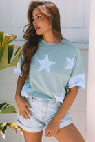 Oversized sage top with frayed sky blue star patches and color-blocked sleeves, styled with shorts.