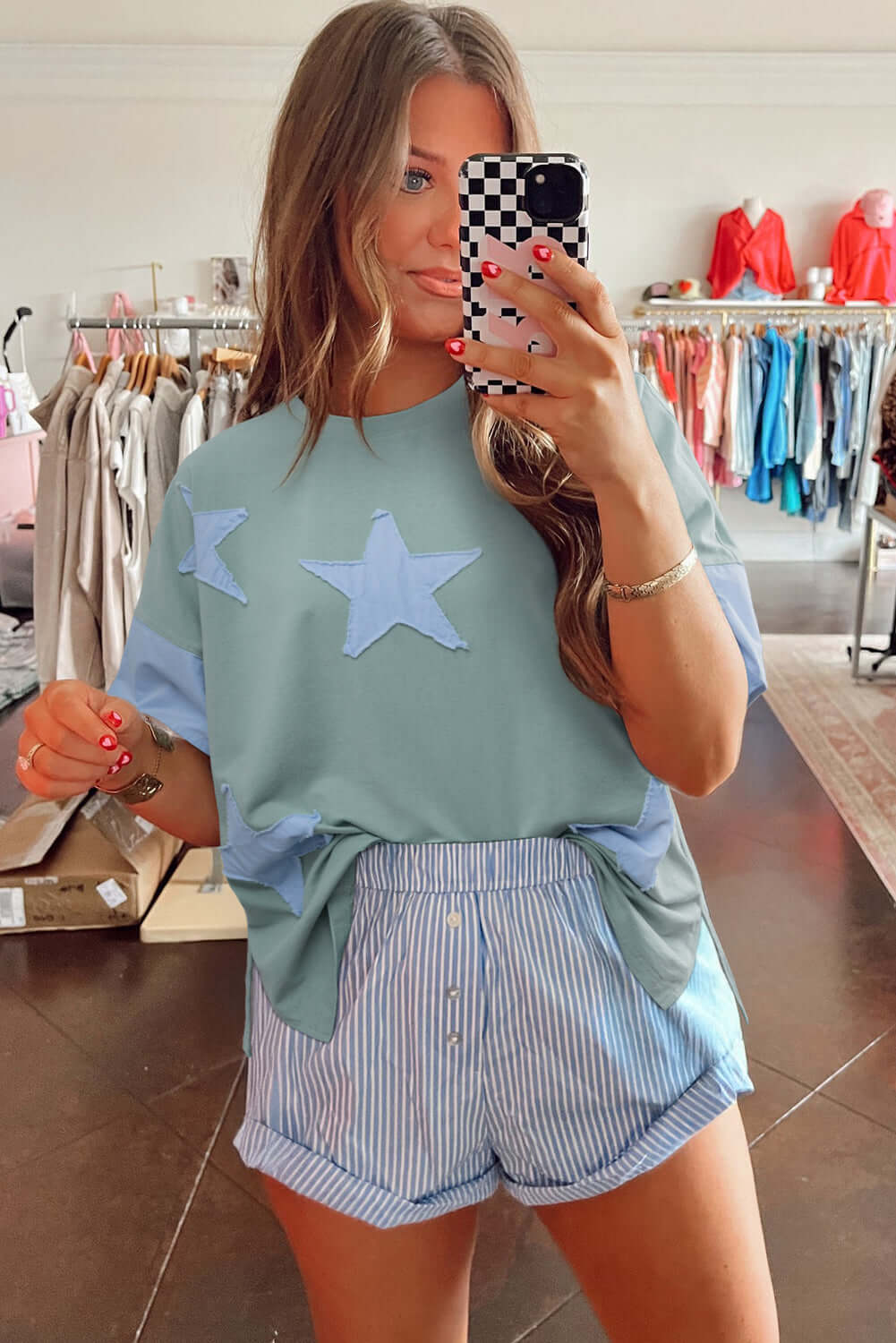 Model showcasing the Cosmic Crush Top in sage with sky star patches and striped shorts, exuding relaxed street style.