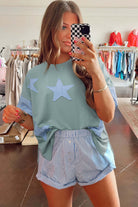 Model showcasing the Cosmic Crush Top in sage with sky star patches and striped shorts, exuding relaxed street style.