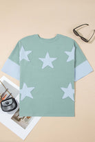 Oversized sage top with frayed sky blue star patches and colorblocked sleeves on a neutral background.
