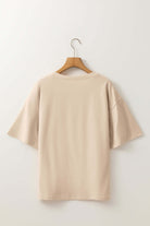 Back view of a beige crochet floral graphic drop shoulder tee on a wooden hanger against a neutral background.