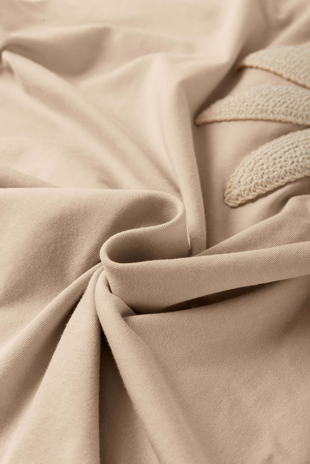 Close-up of soft beige fabric with delicate crochet floral detail, showcasing texture and design elegance.