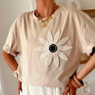 Stylish woman in loose tee featuring crochet daisy graphic, paired with textured white pants for a trendy boho look.