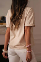 Back view of a woman wearing a beige crochet floral graphic tee styled with trendy bracelets.