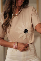 Woman wearing a beige tee with crochet daisy graphic and accessories, showcasing a bohemian style.