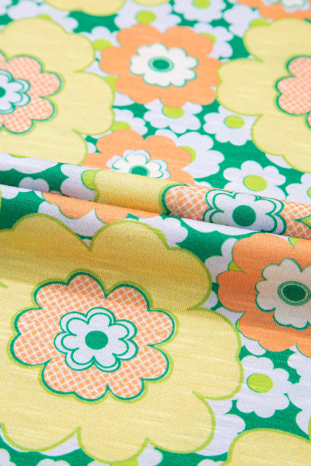 Vibrant floral fabric featuring large yellow and orange flowers on a green background, perfect for summer outfits.