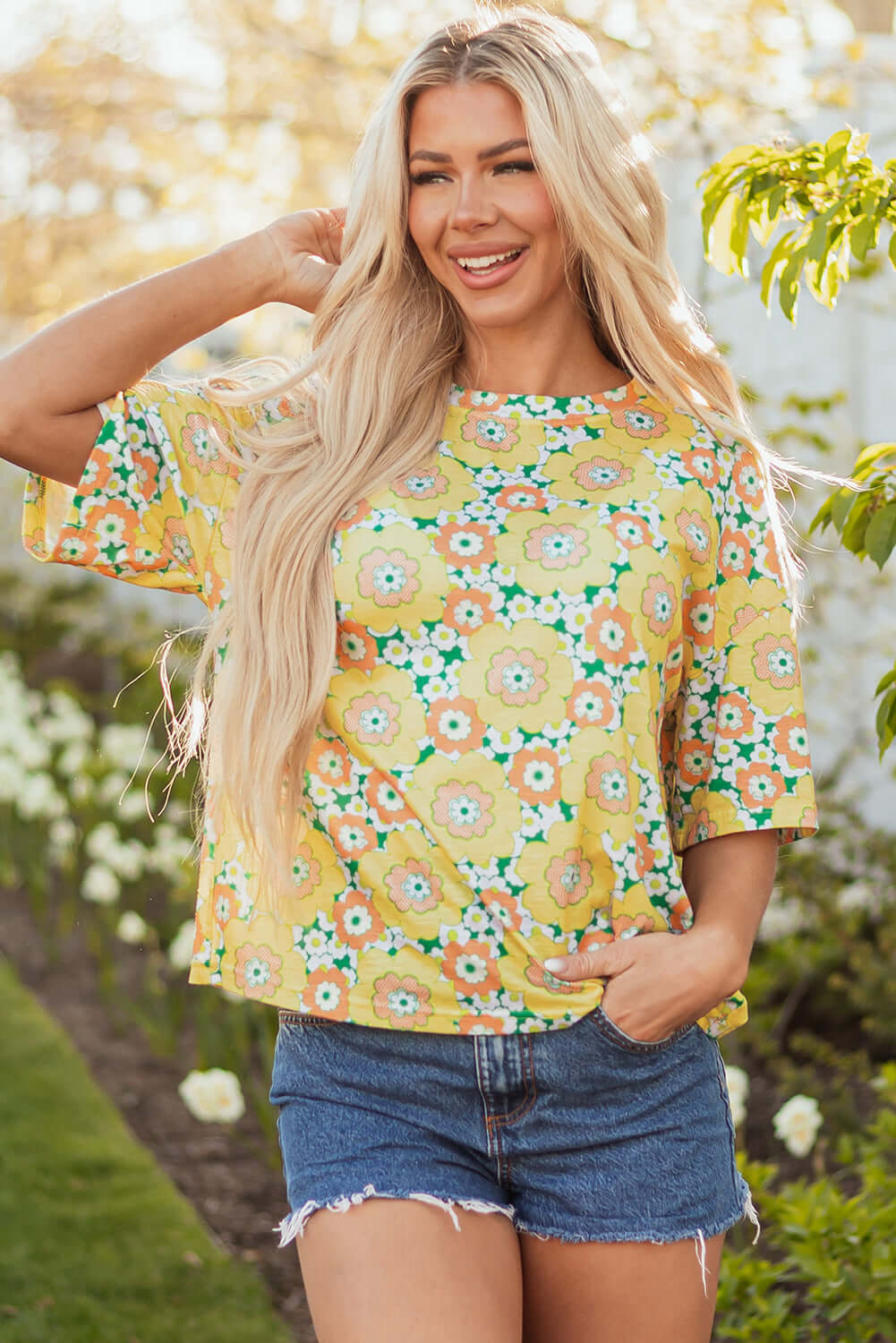 Daisy Disco Top with yellow floral print, styled for summer vibes with denim shorts in a garden setting.