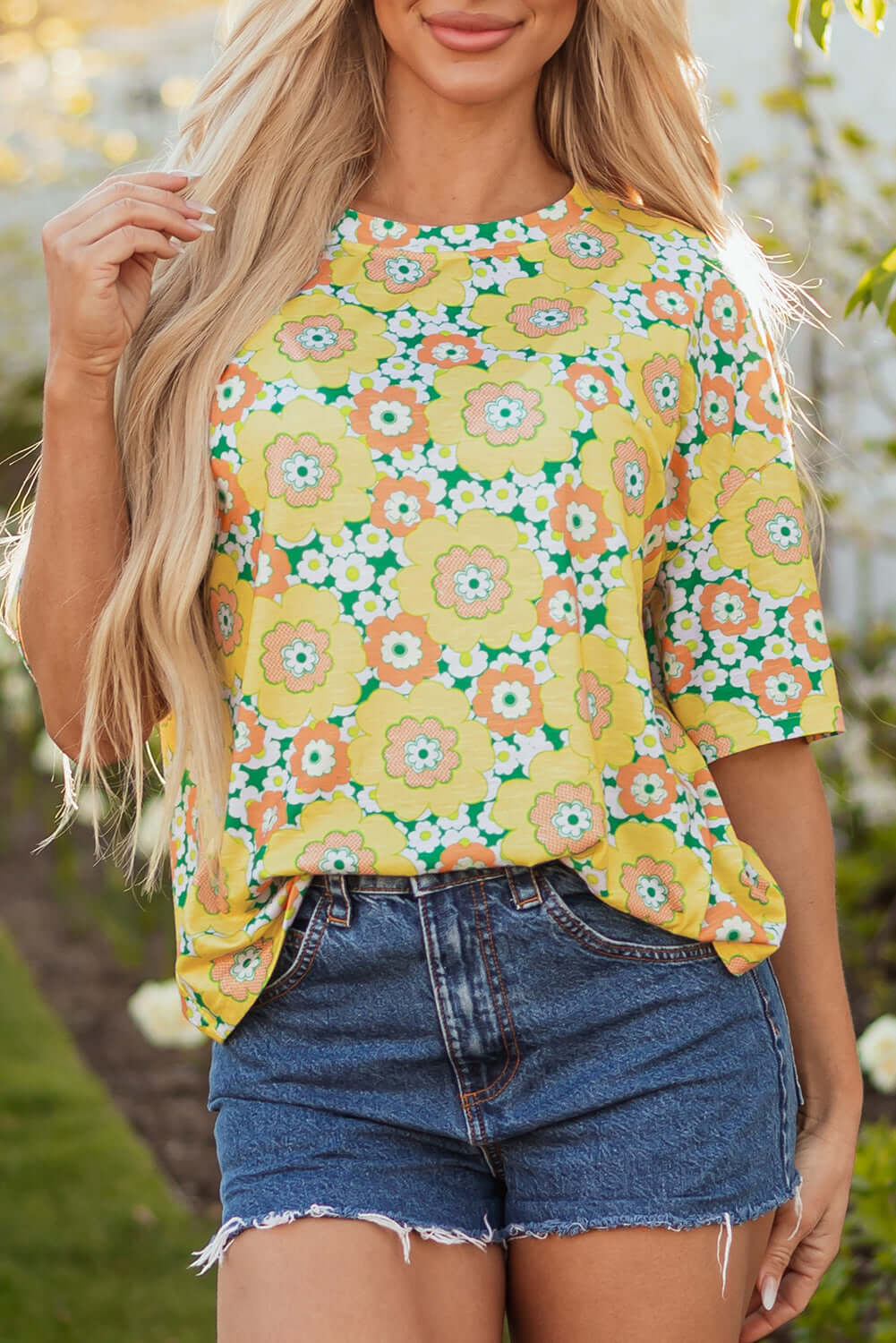 Model wearing a vibrant yellow Daisy Disco Top with floral print, paired with denim shorts, perfect for summer style.