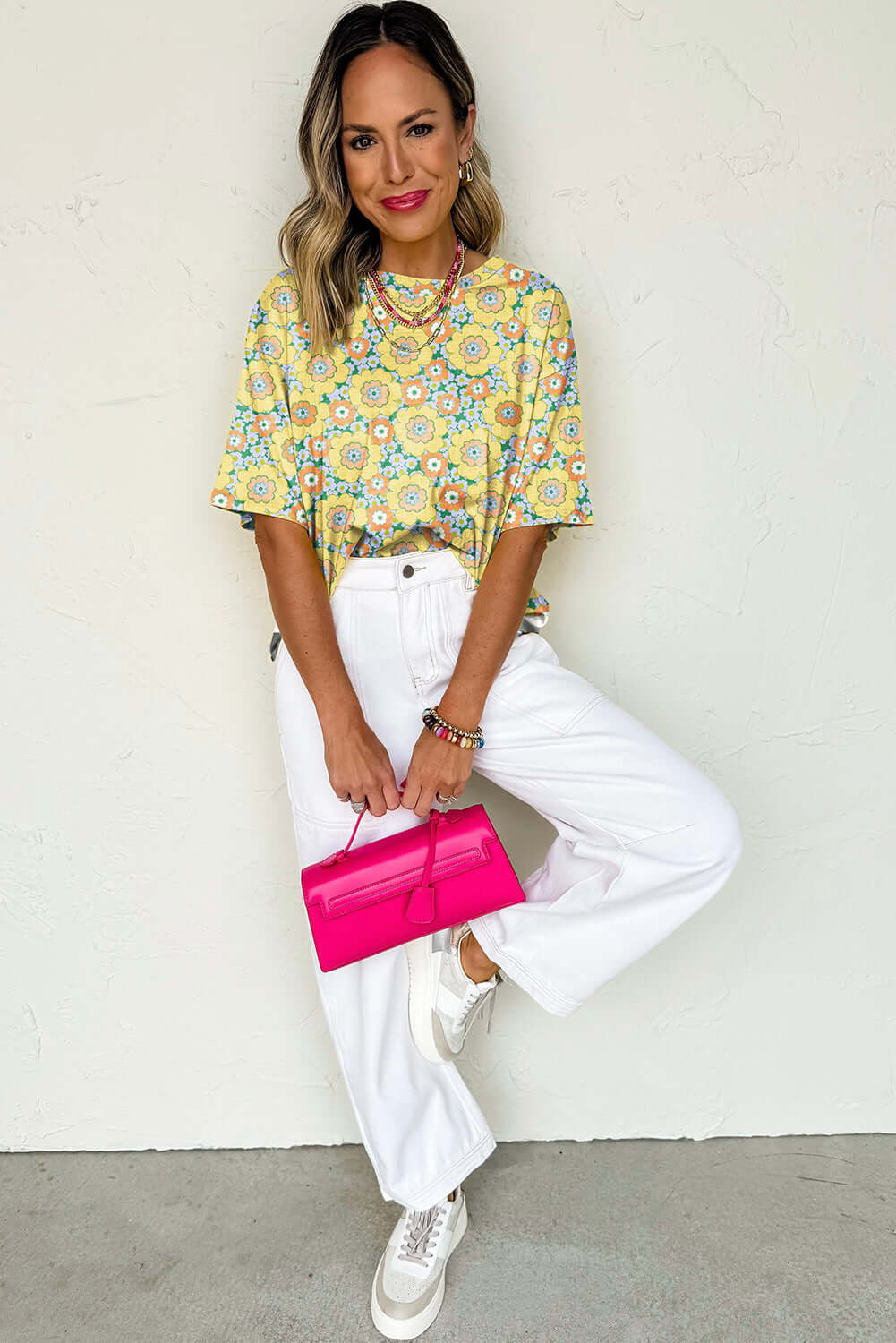 Model wearing Daisy Disco Top with yellow floral print and white wide-leg jeans, holding a pink handbag.