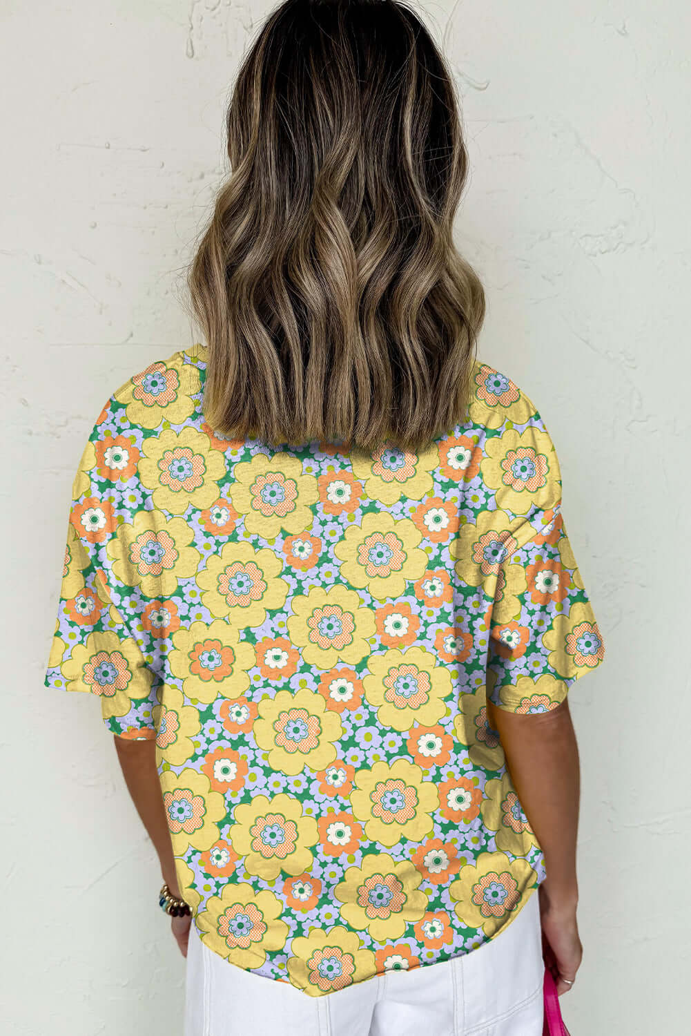 Back view of a woman wearing a yellow floral print Daisy Disco Top with relaxed fit and vibrant flower pattern.