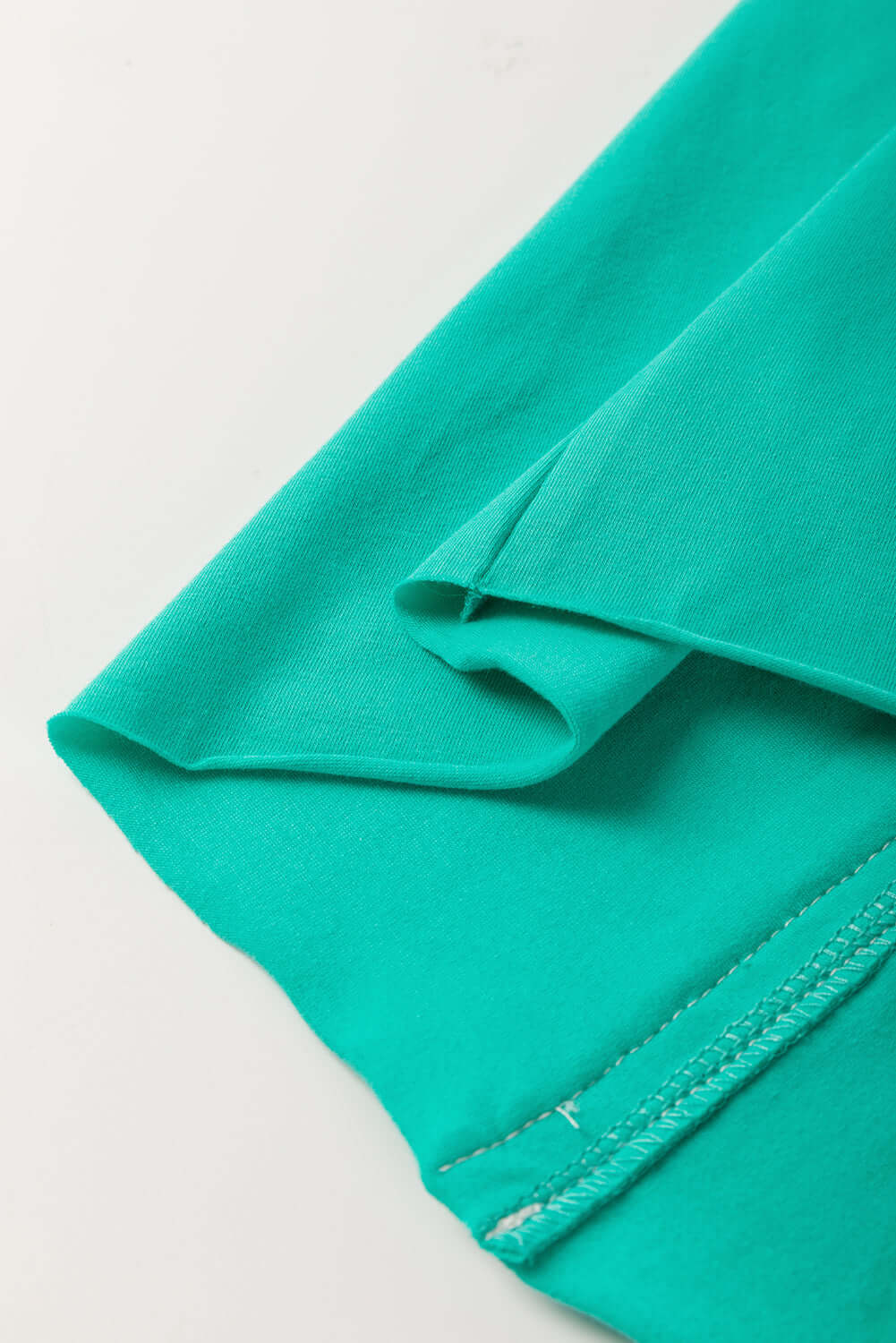 Teal fabric detail of Ribbon Theory Top showcasing smooth texture and raw edge trim.