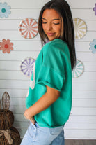Model wearing teal Ribbon Theory Top with lace bow detail, paired with light jeans, smiling against a colorful background.